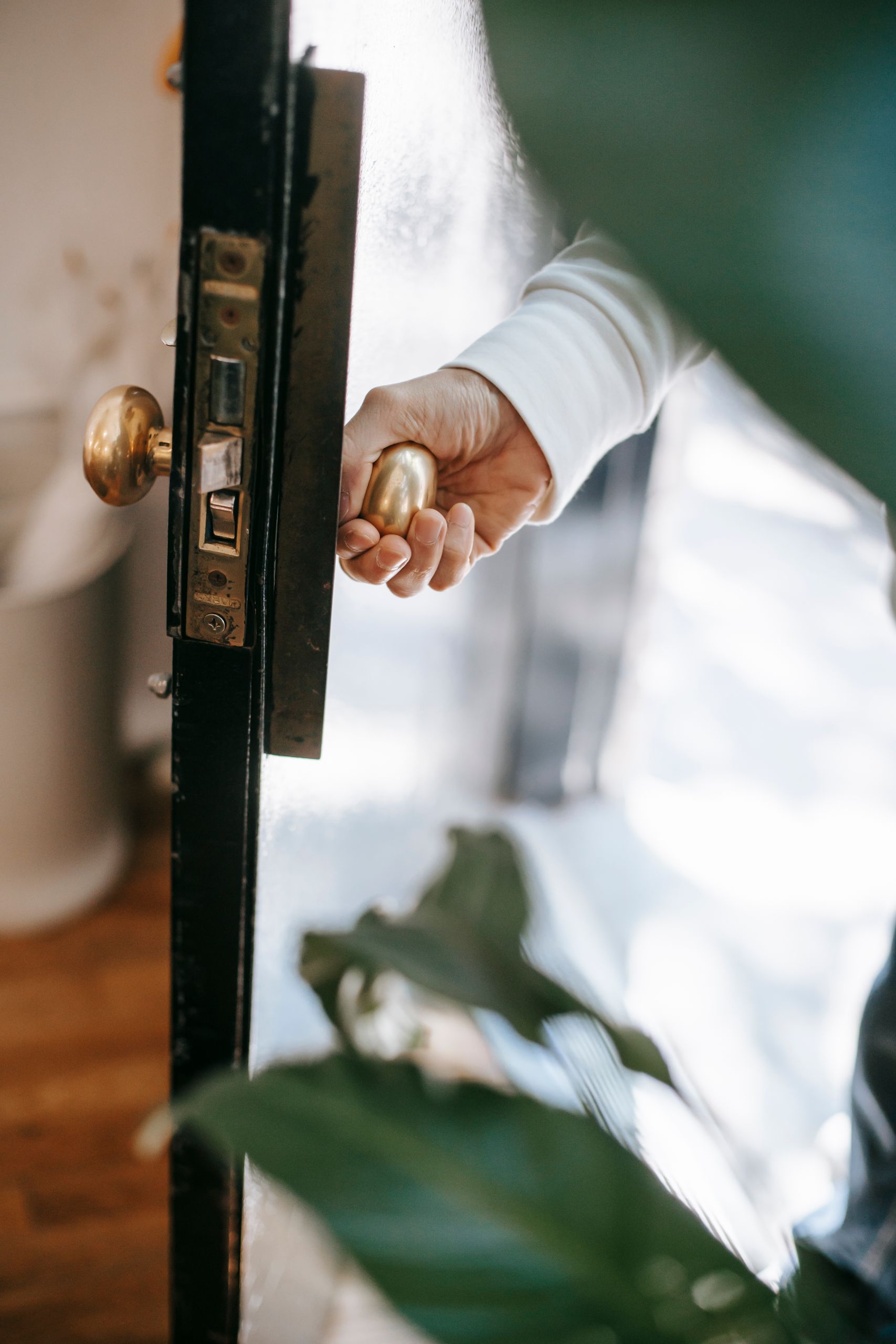 From above of crop anonymous person holding metal door handle while entering house in sunshine